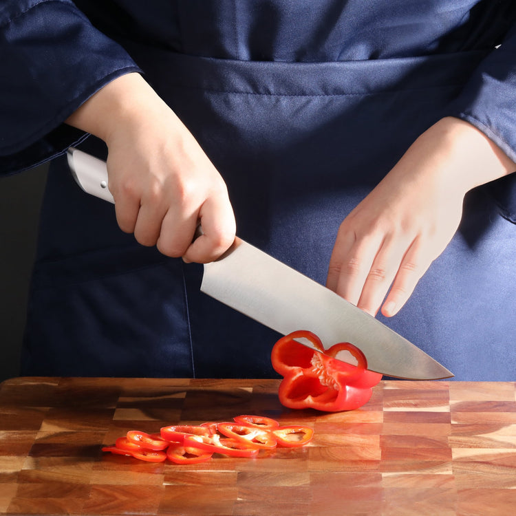 Person slicing a red bell pepper into thin rings on a wooden cutting board with a large kitchen knife.
