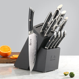 
                    
                      12-piece knife set with black handles in a black angled block, including scissors, displayed on a marble surface.
                    
                  