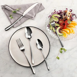 
                    
                      Dinner setting with forged stainless steel flatware including a dinner spoon, fork, and knife on a plate and napkin, next to
                    
                  