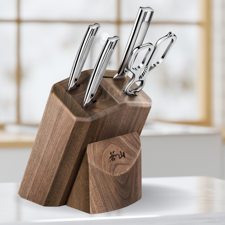 Walnut knife block holding three stainless steel knives and a pair of kitchen scissors on a white surface.