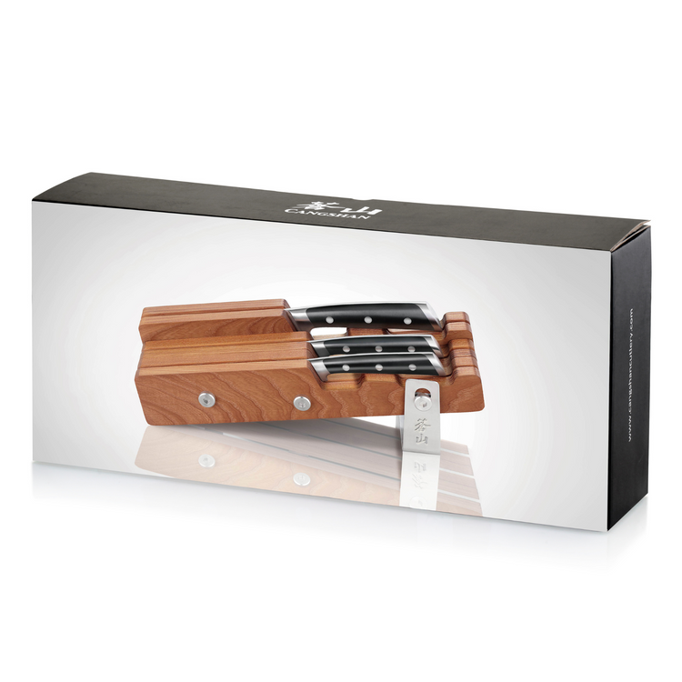 Four knives with black handles in a horizontal ash wood block with metal accents, displayed on product packaging.