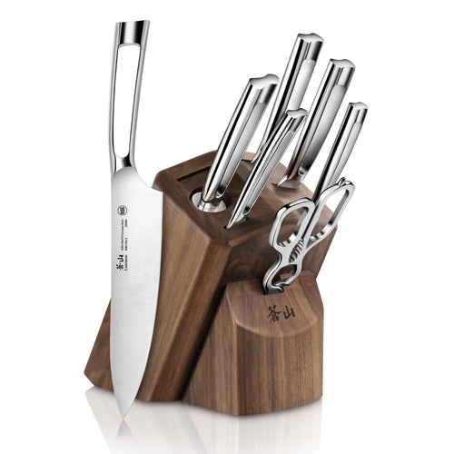 Walnut knife block holding six stainless steel knives and a pair of kitchen shears, with one chef's knife leaning against it.