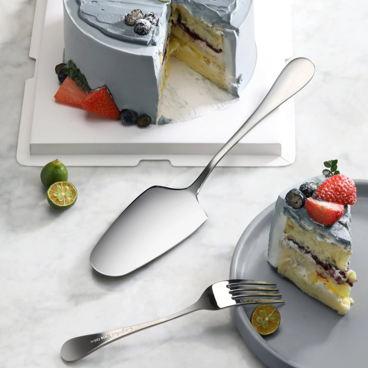 Stainless steel pie server with matte finish handle next to a sliced cake and a fork on a marble surface.