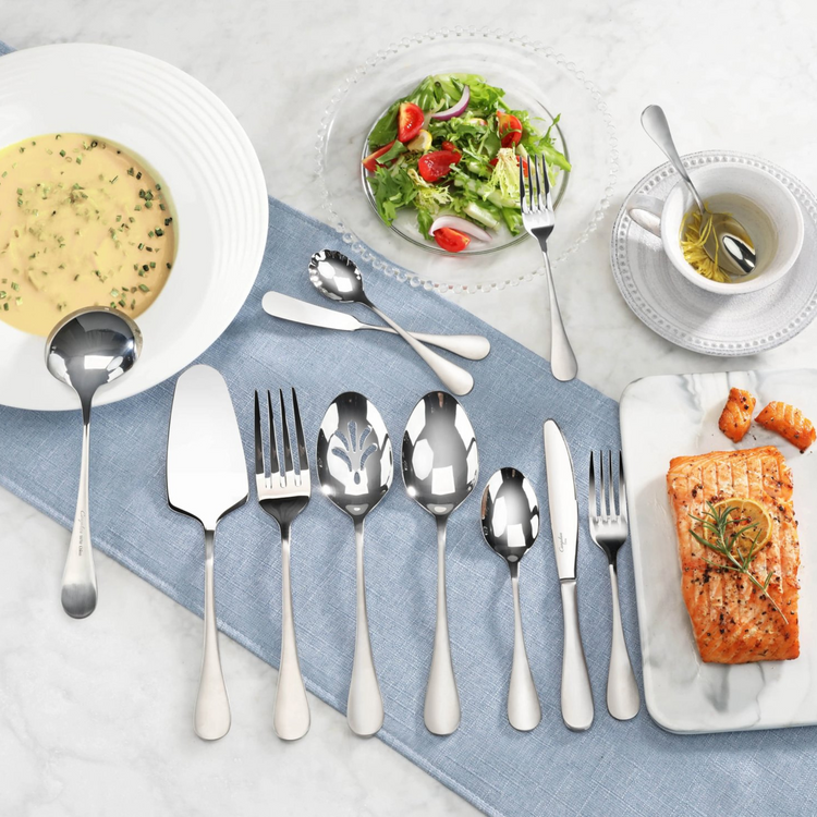 Stainless steel flatware with matte finish handles arranged on a blue cloth, including a soup ladle serving soup.
