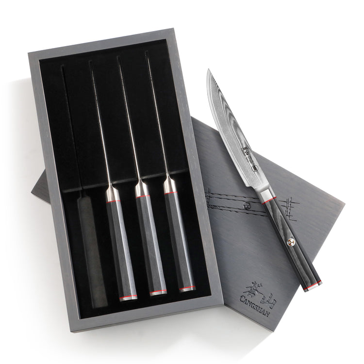 Four steak knives with black handles in a black ash wood box, one knife outside showing a patterned Damascus steel blade.