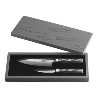 
                    
                      Two Damascus steel knives with black handles displayed in an open gray box with knife illustrations on the lid.
                    
                  