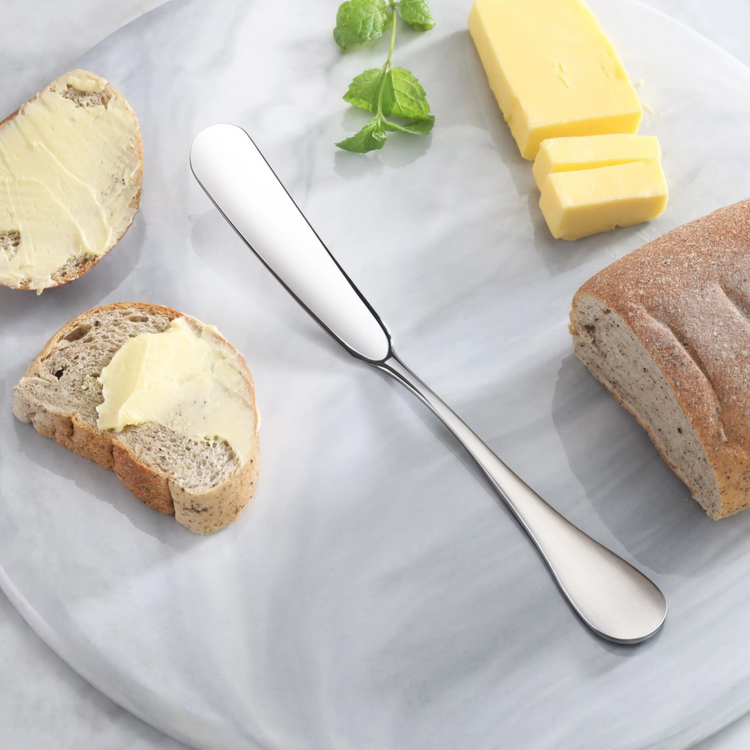 Stainless steel butter knife with matte finish handle on a marble surface with bread, butter, and mint leaves.