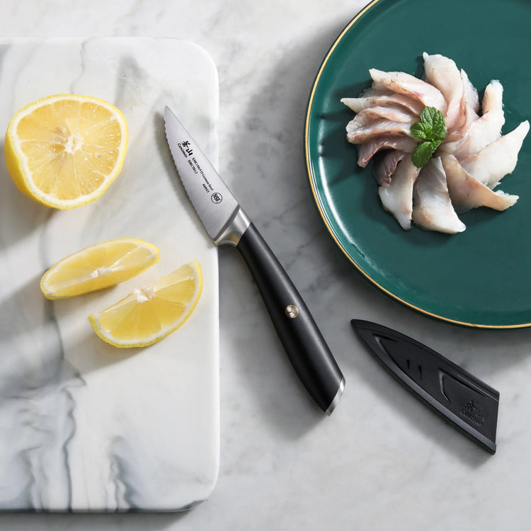 Black-handled fillet knife with sheath on marble surface next to sliced lemon and fish fillets on green plate.
