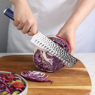 
                    
                      Hand holding a knife slicing a halved purple cabbage on a wooden cutting board next to a bowl of salad.
                    
                  