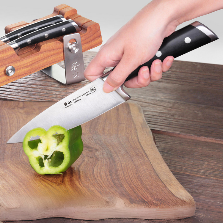 Hand holding a knife from a wooden block set, slicing a green bell pepper on a wooden cutting board.