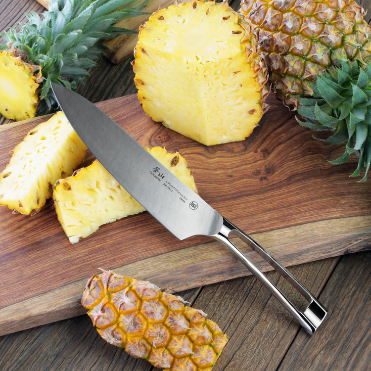 Chef's knife with stainless steel handle on wooden cutting board next to sliced pineapple pieces.