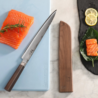 
                    
                      Walnut magnetic knife sheath next to a Japanese-style knife and salmon on a cutting board and slate plate.
                    
                  