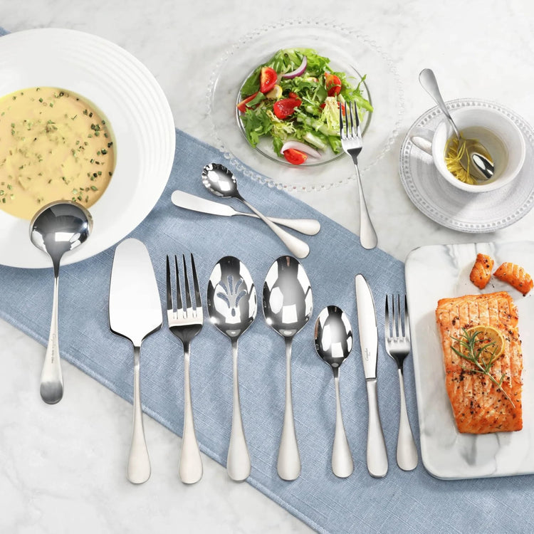 Set of stainless steel flatware with matte finish handles displayed on a blue cloth, alongside soup, salad, and salmon dishes