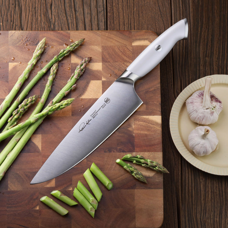 8-inch chef's knife with silver handle on wooden cutting board next to asparagus and garlic bulbs on plate