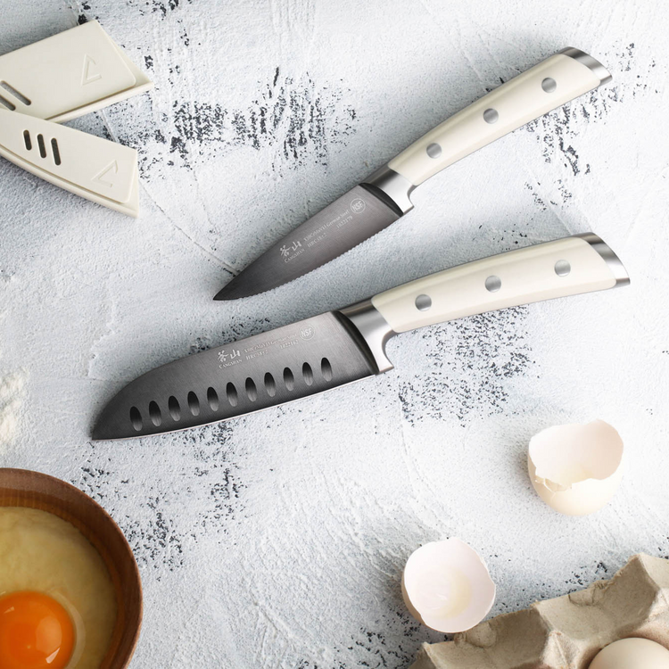 Two kitchen knives with white handles on a textured surface, near an egg in a bowl and broken eggshells.
