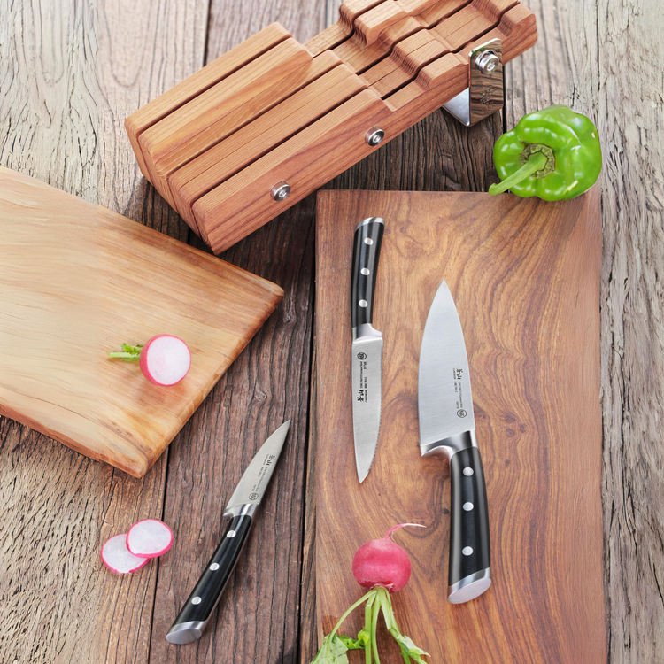 Two kitchen knives with black handles on a wooden cutting board, a wooden knife block, radishes, and a green bell pepper.