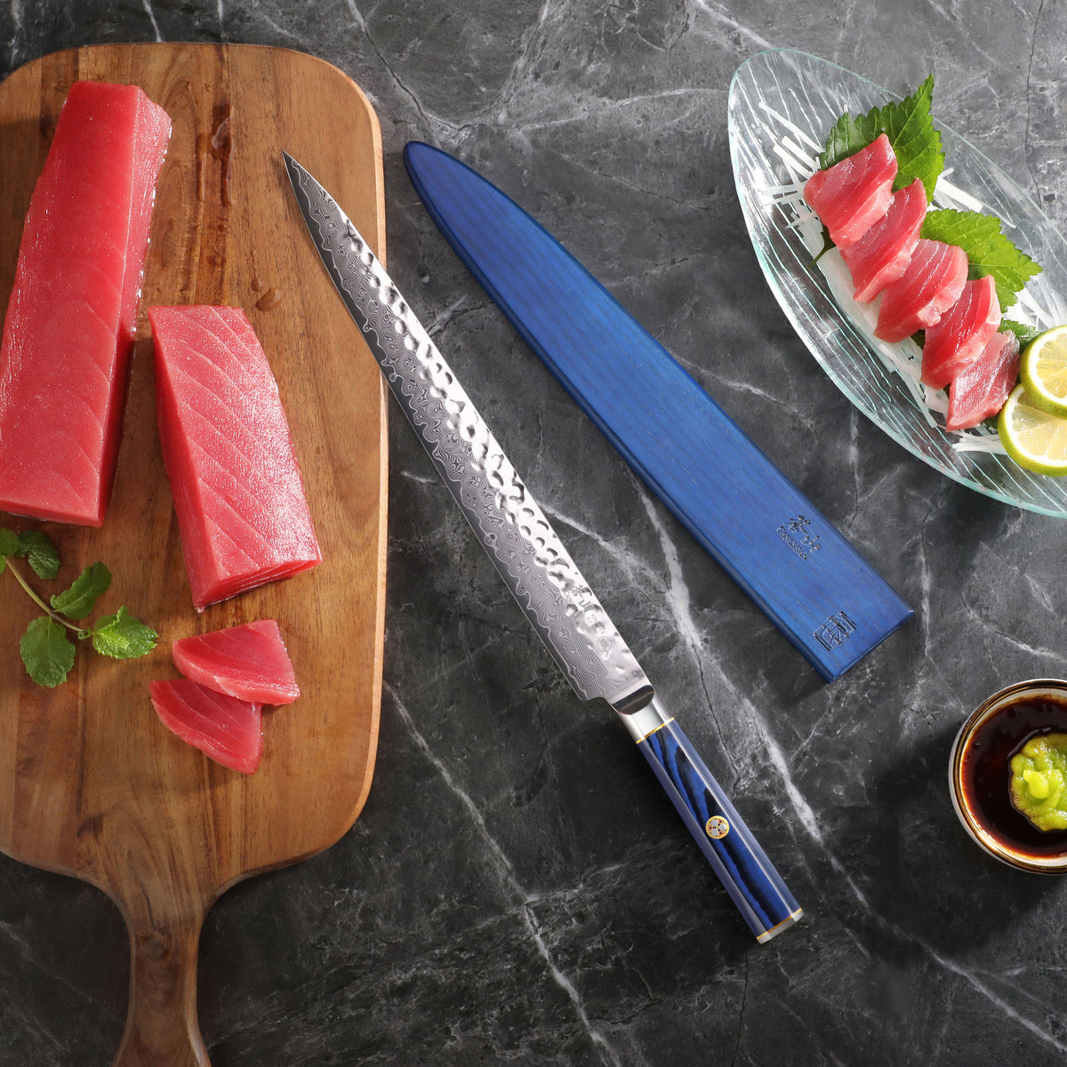 12-inch sashimi knife with blue sheath on marble surface, next to sliced tuna on wooden board and sashimi plate with soy sauc