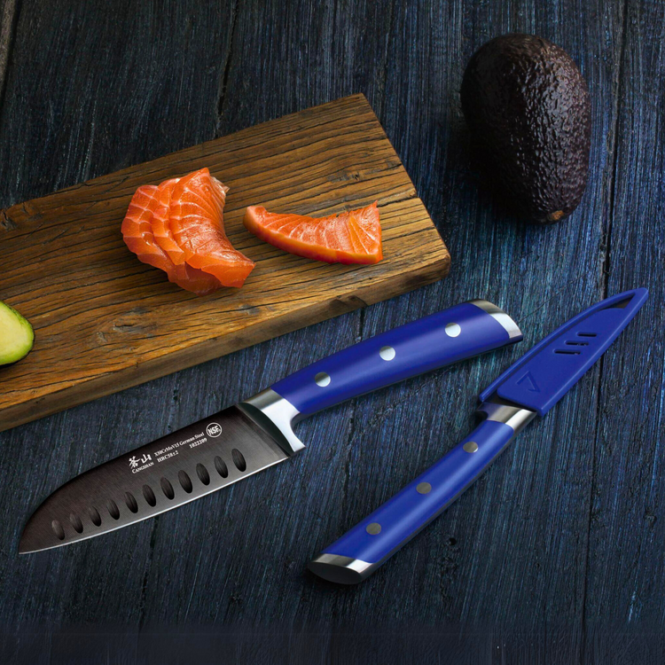 Slices of salmon on a wooden board with a whole avocado and a blue-handled knife on a dark surface.