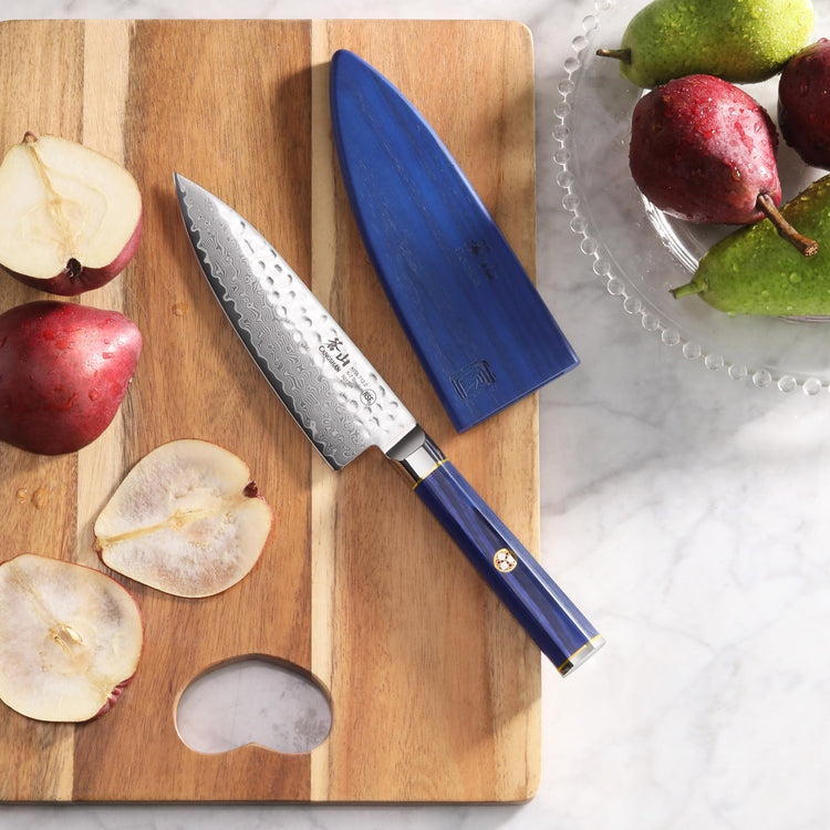 6-inch chef's knife with blue handle and sheath on wooden cutting board with sliced pears and whole pears nearby.