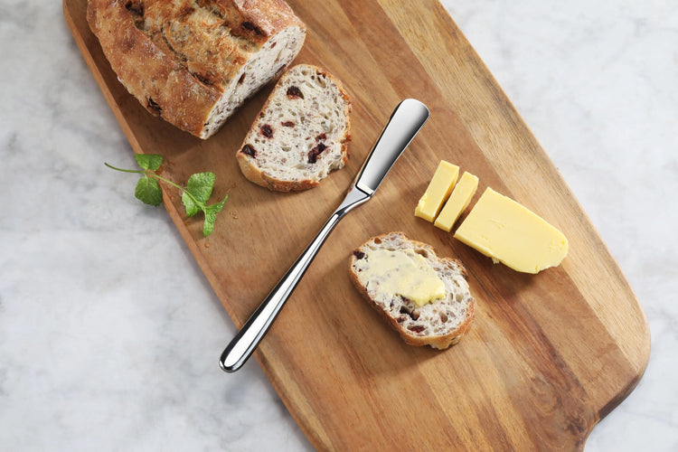 Butter knife with mirror finish on wooden board with sliced bread and butter.