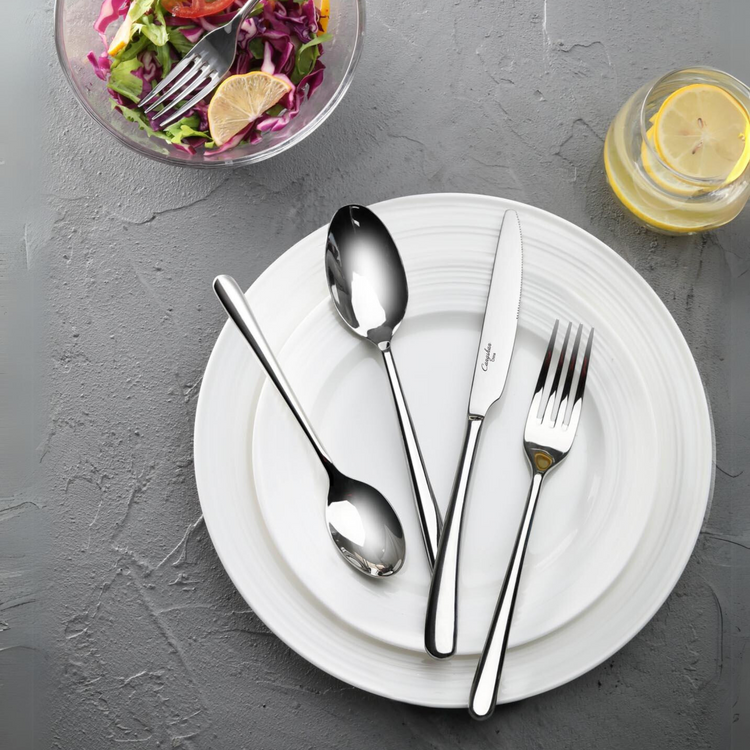 Four pieces of stainless steel flatware—a fork, knife, tablespoon, and teaspoon—rest on a white plate.