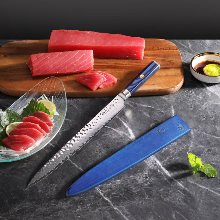 KITA Series 12-inch sashimi knife with blue handle and sheath, next to sliced raw tuna on a wooden board and in a glass dish.