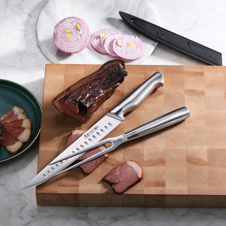 Two stainless steel carving knives on a wooden cutting board with sliced smoked meat and a plate of sliced red onion.