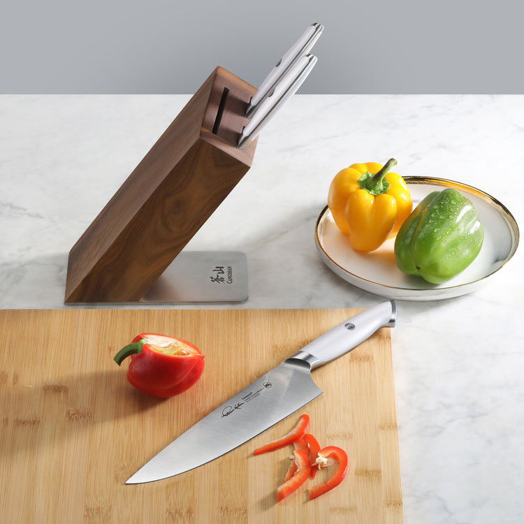 Knife block with two knives inserted, one chef's knife on a cutting board with sliced red bell pepper, and a plate holding ye