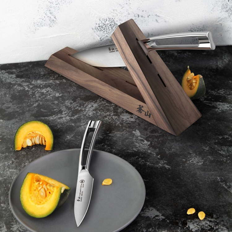 Walnut wood knife block holding a chef's knife, with a paring knife on a plate next to sliced squash.