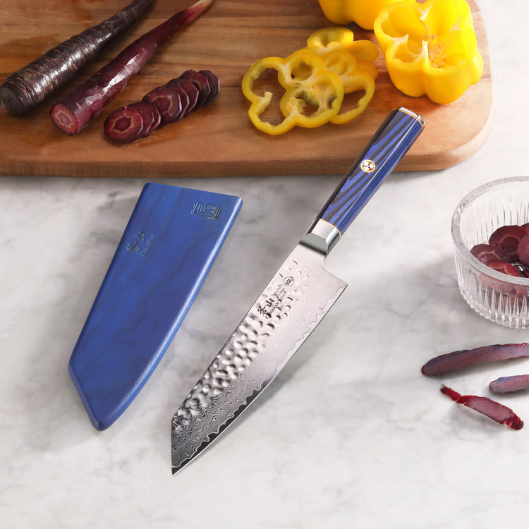 7-inch Kiritsuke knife with blue handle and sheath on marble surface, sliced vegetables and cutting board in background