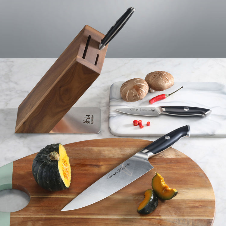 Knife block set with two knives, one on a wooden cutting board with sliced squash, and one on a marble board with mushrooms a
