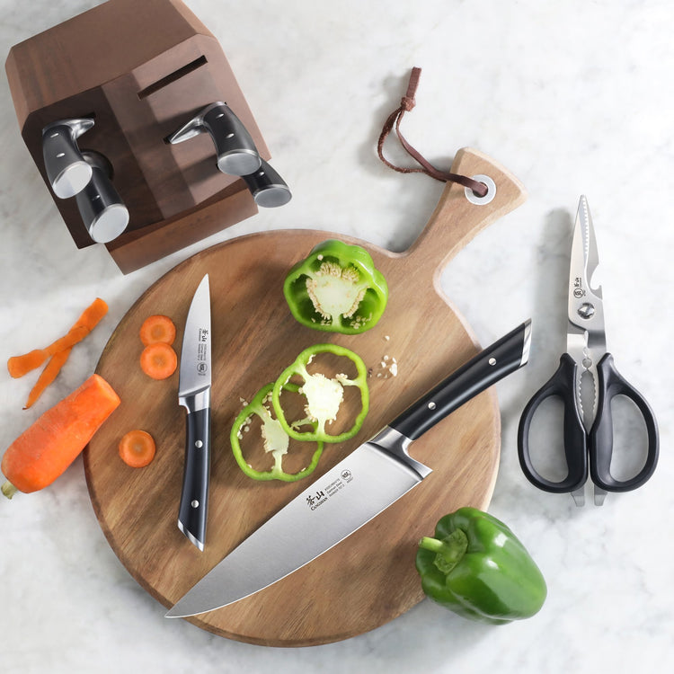 Knife block with four knives, two cutting boards with sliced green bell pepper and carrot, and kitchen scissors on a marble s