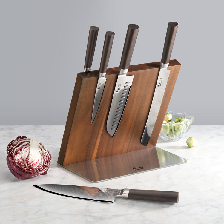 Six kitchen knives with dark handles in a wooden and metal magnetic block, with a cabbage and a bowl of Brussels sprouts near