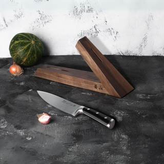 
                    
                      Walnut wood triangular knife block with a chef's knife and small vegetables on a dark surface.
                    
                  