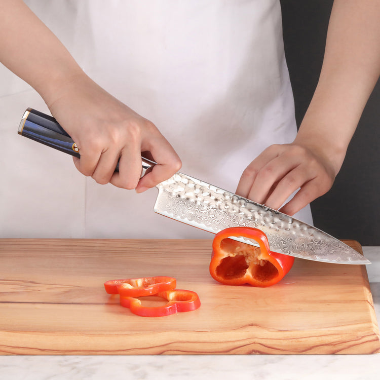 Person slicing a red bell pepper on a wooden cutting board with a blue-handled chef's knife.