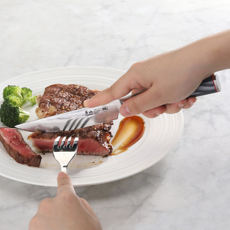 Hand holding a steak knife cutting a medium-rare steak on a white plate with broccoli and sauce.