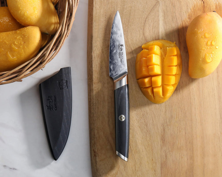 AIRA Series 3.5-inch Paring Knife with Damascus steel blade on a wooden cutting board next to diced mangoes and a black