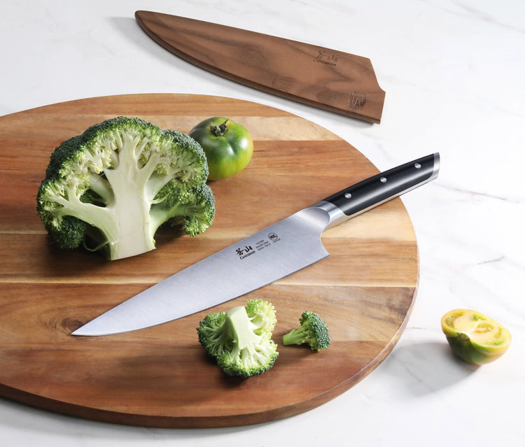 8-inch chef's knife with black handle on wooden cutting board next to cut broccoli and green tomato, with wooden sheath nearb