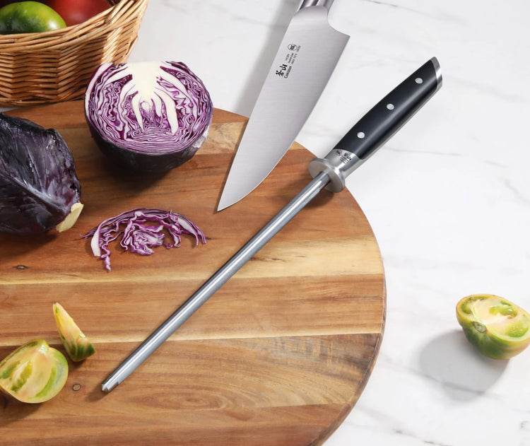 9-inch honing steel with black handle and knife on wooden cutting board next to sliced purple cabbage and green tomatoes.