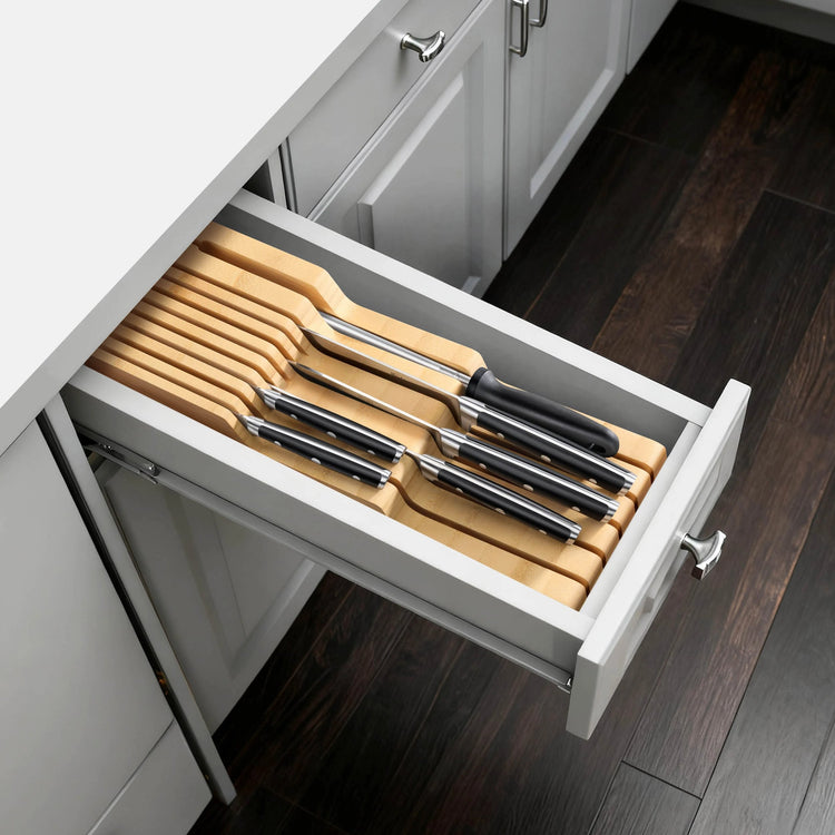 Seven knives with black handles neatly arranged in a wooden in-drawer organizer inside a kitchen cabinet drawer.