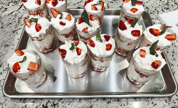 Multiple small glass jars filled with strawberry shortcake desserts topped with whipped cream, sliced strawberries, and