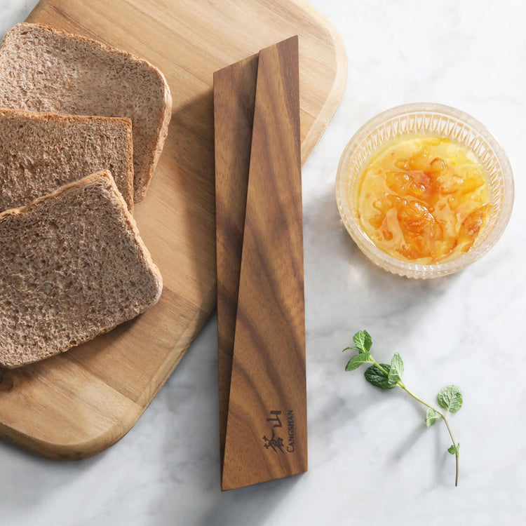 Ash wood magnetic knife sheath resting on a wooden cutting board next to sliced bread, a bowl of marmalade, and a sprig of mi