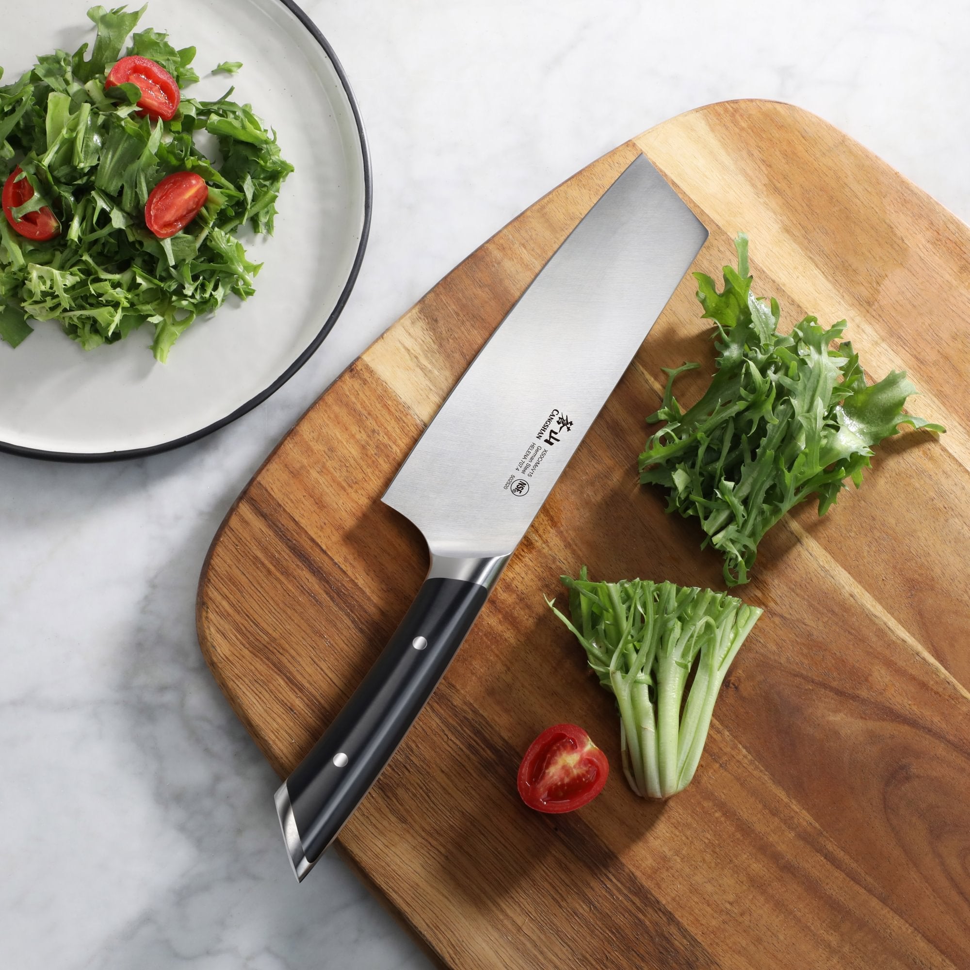 7-inch Nakiri knife with black handle on wooden cutting board next to chopped greens and halved cherry tomato.