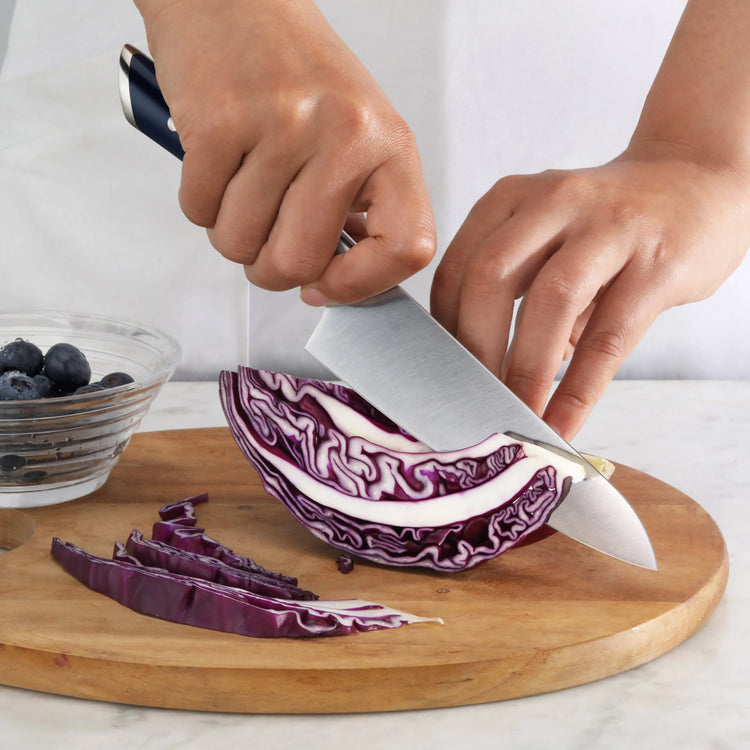 Hands slicing a wedge of purple cabbage on a wooden cutting board with a utility knife.