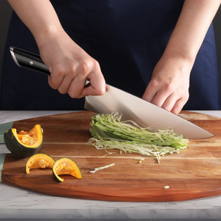 
                    
                      Hands slicing shredded cabbage on a wooden cutting board with a chef knife, next to cut pieces of squash.
                    
                  