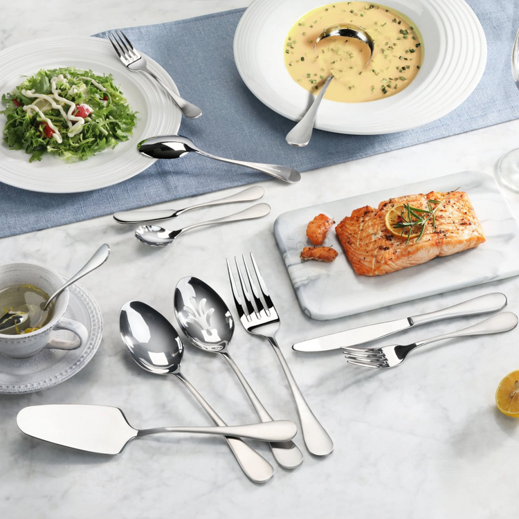 Stainless steel flatware set with matte finish handles displayed with salad, soup, salmon, and tea on marble surface.