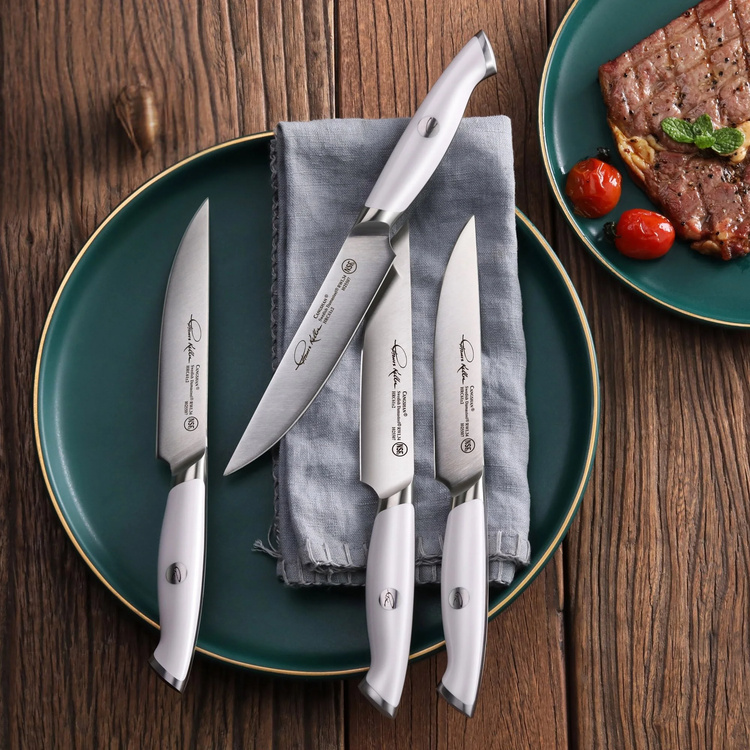 Four white-handled steak knives with engraved blades arranged on a green plate with a gray napkin on a wooden surface.