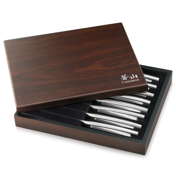 Wooden box partially open displaying eight stainless steel steak knives with straight edges arranged in a black foam insert.