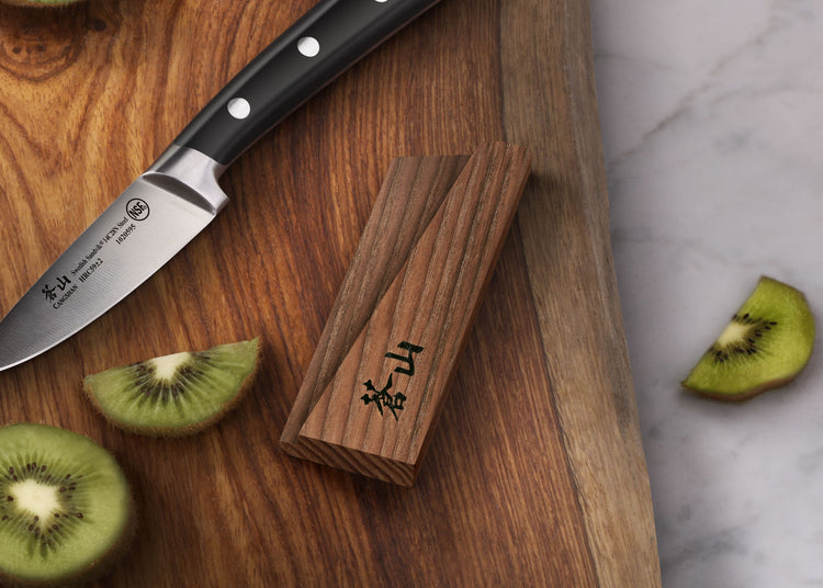 Solid ash wood magnetic knife sheath placed on a wooden cutting board next to a paring knife and sliced kiwi.