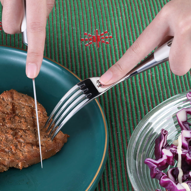 Hand holding a stainless steel fork piercing a cooked steak on a green plate, with a knife cutting the steak.